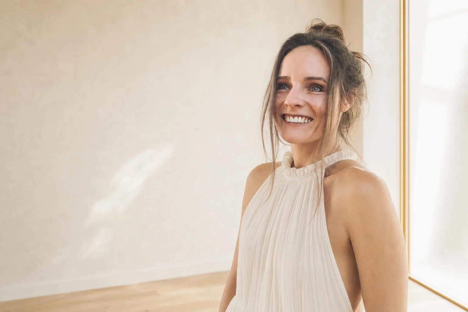 Hannah Steinrock in einem hellen, fast leeren Raum, das Haar zu einem lockeren Dutt gesteckt, lachend an der Kamera vorbeiblickend.